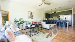 Ein modernes Wohnzimmer mit einer Couch, einem Couchtisch und einem Essbereich mit Stühlen, im Hintergrund eine Küche.