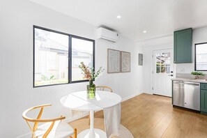 Eine moderne Küche mit Geschirrspüler, ein Essbereich mit rundem Tisch und Stühlen sowie ein großes Fenster mit Außenblick.
