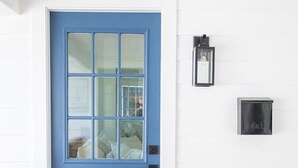 Une porte bleue avec une fenêtre, un luminaire fixé au mur et un thermostat.