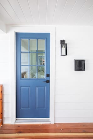 Eine blaue Tür mit Fenster, einer Wandleuchte und einem Thermostat.