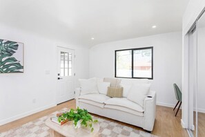 Una sala de estar moderna con un sofá blanco, una mesa de centro con una planta, un cuadro en la pared y una ventana con vistas.
