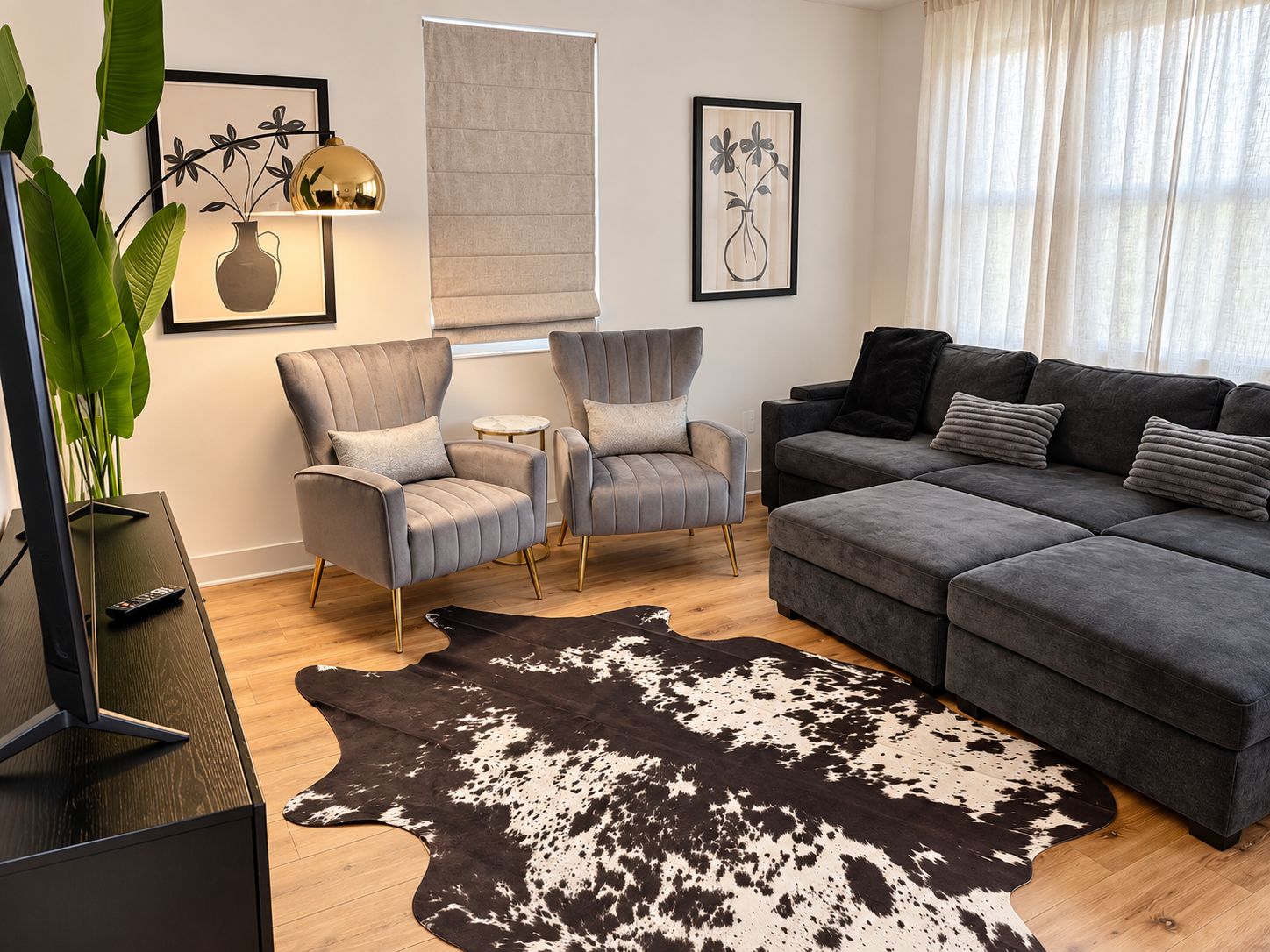 A modern living room with a grey sofa, two armchairs, a cowhide rug, and framed artwork on the walls.