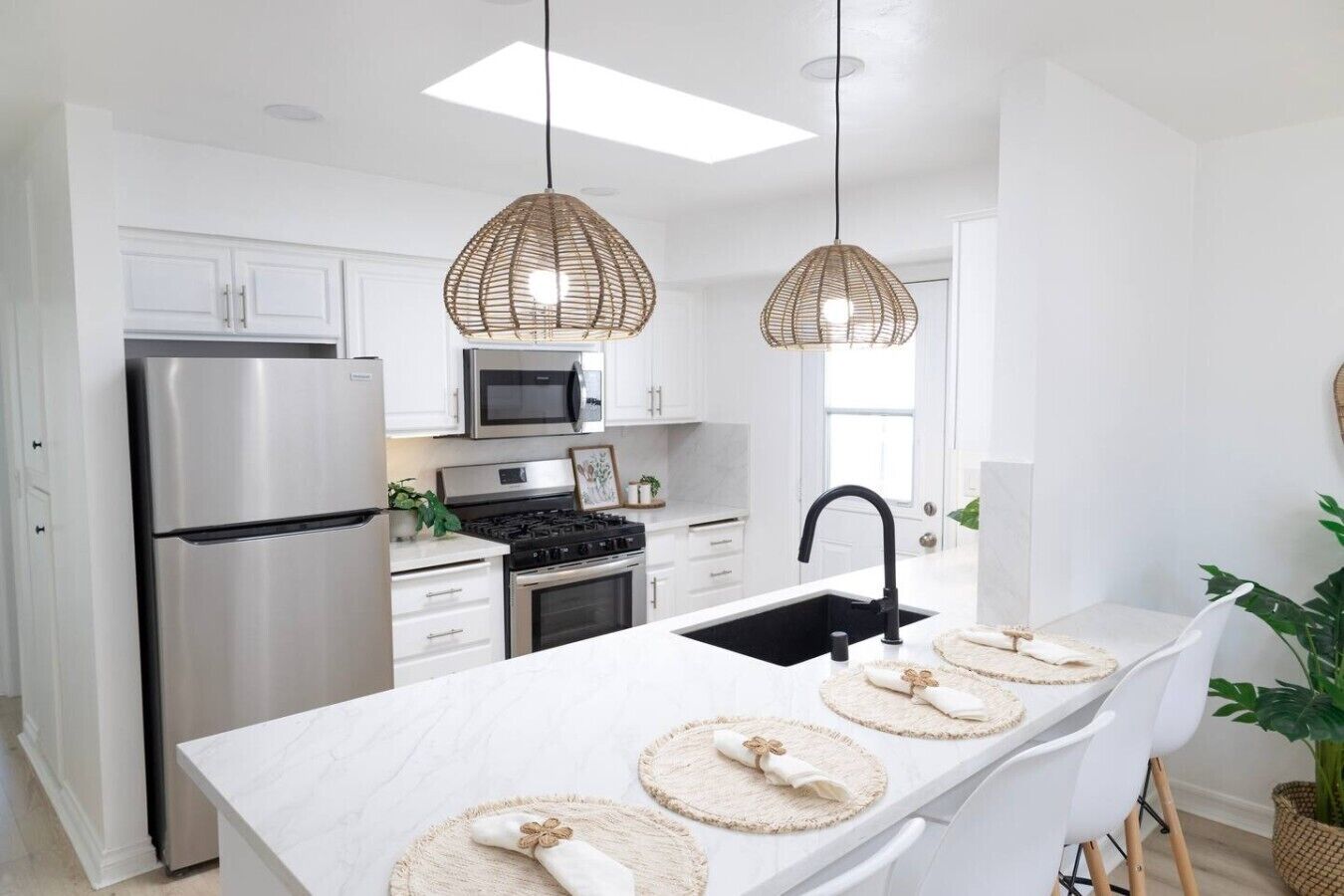 A modern kitchen with white cabinetry, stainless steel appliances, a black sink, and woven pendant lights.