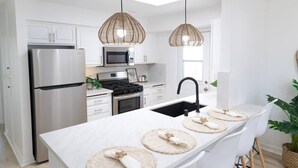 A modern kitchen with white cabinetry, stainless steel appliances, a black sink, and woven pendant lights. - The Orkney - A Modern Coastal Cardiff Residence (Encinitas)