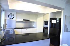 Eine moderne Küche mit weißen Schränken, einer schwarzen Arbeitsplatte, einem Edelstahl-Spülbecken, einer Uhr und einem Kühlschrank.