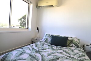 Ein Schlafzimmer mit einem Bett, einem Nachttisch, einer Lampe und einer Klimaanlage.