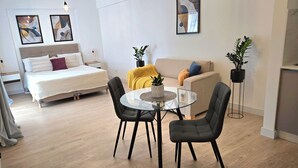 Uma sala de estar moderna com uma cama, sofá, mesa redonda de vidro e duas cadeiras.