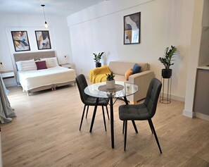 Una sala de estar moderna con una cama, un sofá, una mesa redonda de vidrio y dos sillas.