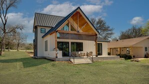 A modern two-story house with a large front porch, a covered outdoor seating area, and a spacious backyard.