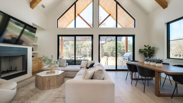 A spacious living area with a fireplace, a large sofa, a dining table, and a kitchen visible through a glass door.