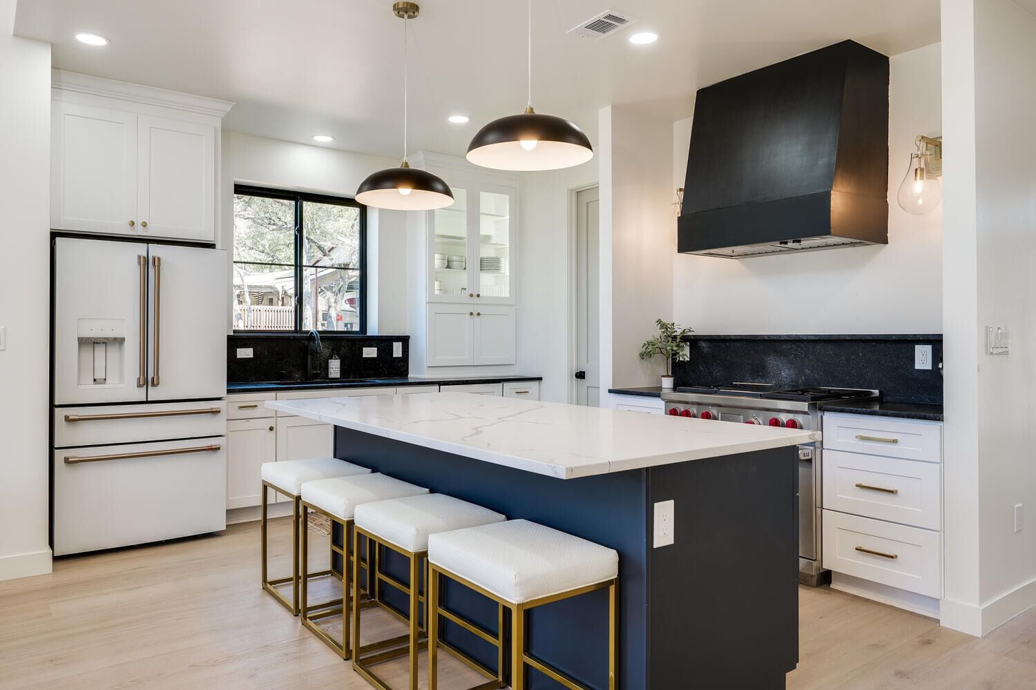 Une cuisine moderne avec des meubles blancs, un grand îlot central doté de tabourets, une hotte noire et des luminaires suspendus.