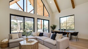 A spacious living area with a sectional sofa, a dining table, and large windows offering views of trees.