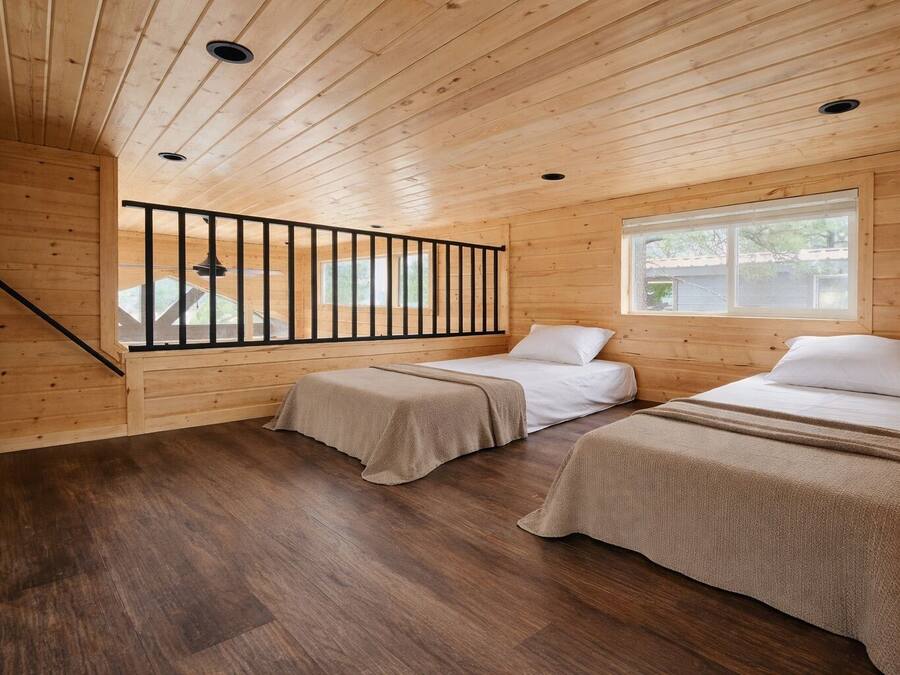 A cabin with two beds, wooden walls, a window, and a staircase.