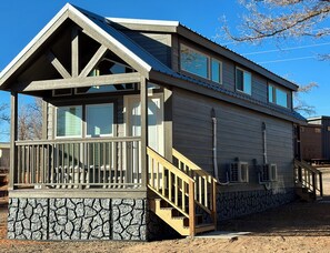 A two-story house with a stone foundation, a balcony with a railing, and a staircase leading to the upper floor. - Cozy Tiny Home with Loft Sleeps 6 (Page)