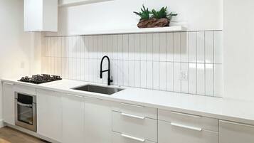 A modern kitchen with white cabinetry, a stainless steel sink, and a built-in stove.