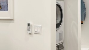 A laundry room with stacked washers and dryers, a wall-mounted control panel, and a door. - masterfully blend modern luxury studio with thoughtful details (Los Angeles)