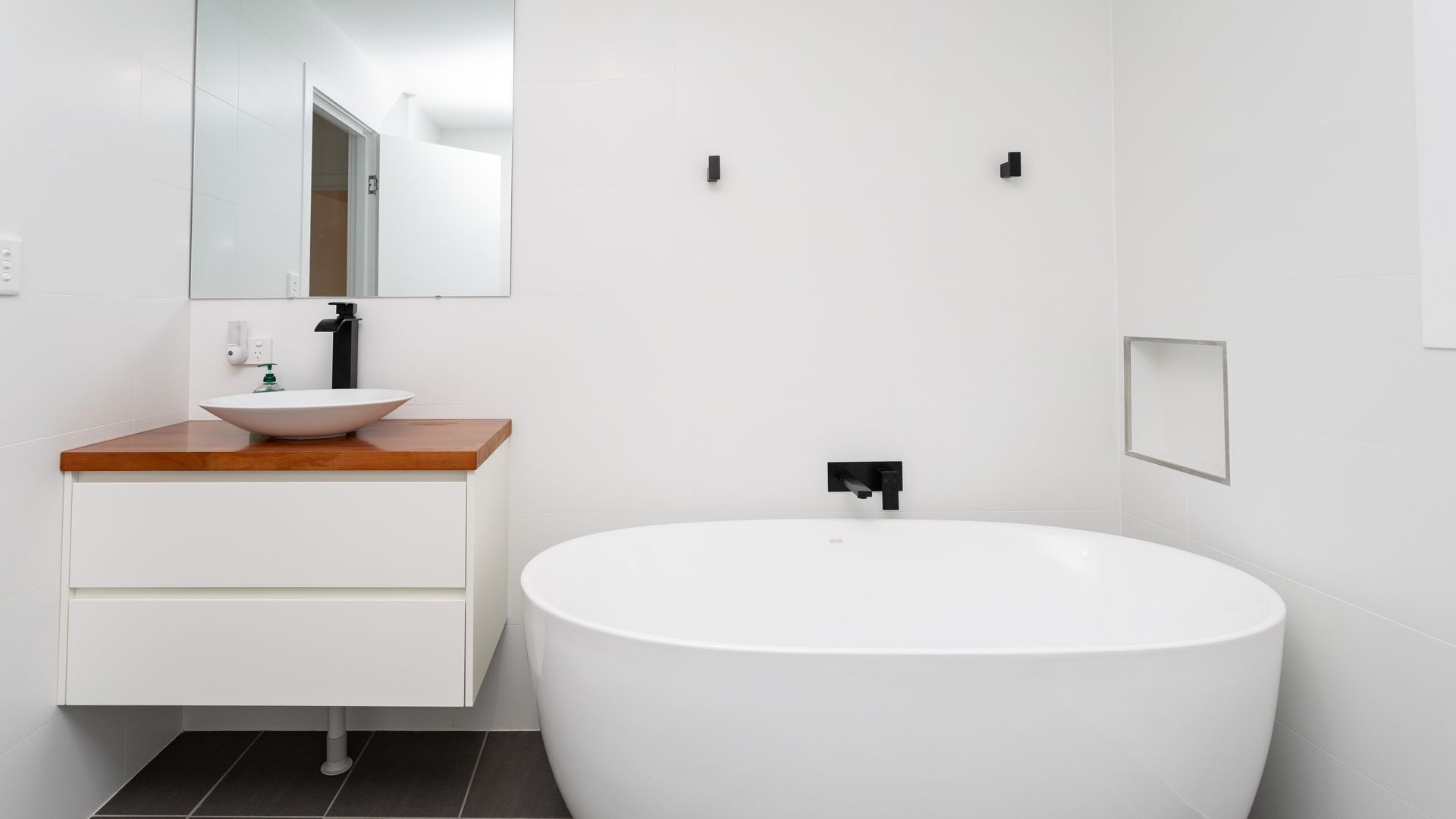 Ein modernes Badezimmer mit einer freistehenden Badewanne, einem Holztischchen, einem weißen Waschbecken und einem Spiegel.