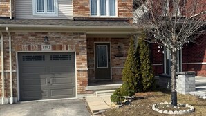 A two-story house with a garage, a welcome sign, and a small tree in the front yard. - Modern Private Suite with 100 inch TV Quiet Oshawa (Oshawa)