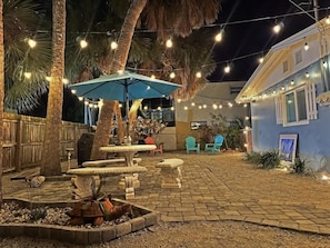 Un espace extérieur aménagé en terrasse, avec des guirlandes lumineuses, un parasol bleu et du mobilier de jardin.