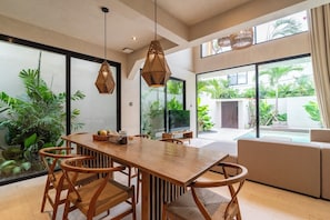 Uma área de refeições moderna com mesa de madeira, cadeiras de vime e iluminação pendente.