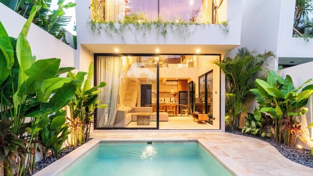 Ein modernes Haus mit Pool, Essbereich und Wohnzimmer, die durch große Glasüren sichtbar sind.