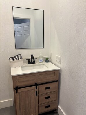 A bathroom with a white sink, a mirror, a towel rack, and a wooden cabinet with drawers. - Relax and recharge private studio in Indio, CA (Indio)