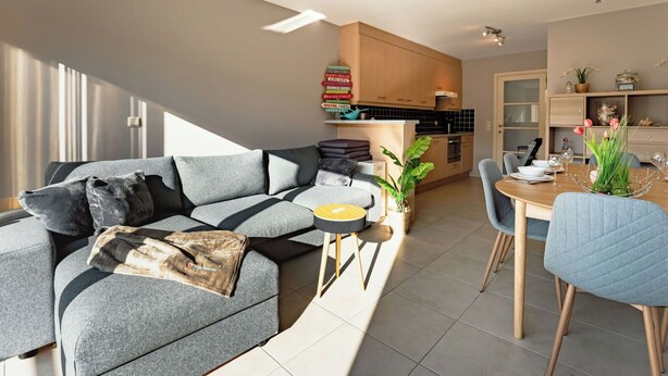 En moderne opholdsstue med sofa, spisebord, stole og et køkkenområde.