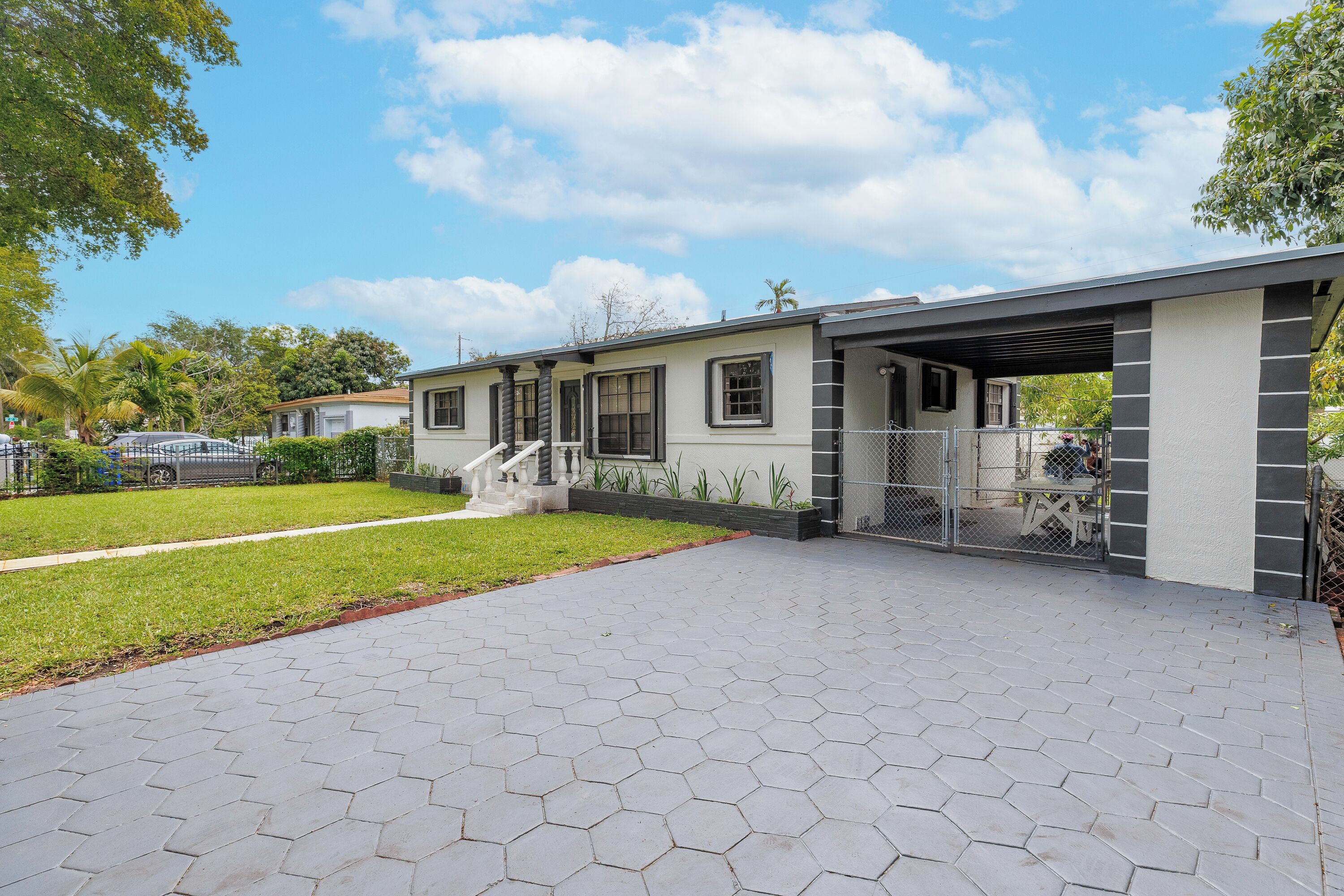 Una propiedad residencial con un porche cubierto, un camino de entrada con baldosas hexagonales y un patio trasero cercado.