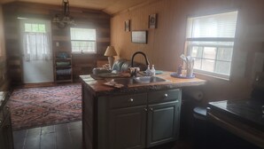 A kitchen with a sink, stove, and a dining area with a chair and table. - Sweet county cabin in the cozy county (Jennings)