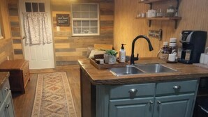 A cozy kitchen with a central island, wooden cabinets, a rug, and a coffee sign. - Sweet county cabin in the cozy county (Jennings)