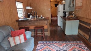A compact kitchen with wooden cabinetry, a central island, and a dining area with a sofa and rug. - Sweet county cabin in the cozy county (Jennings)