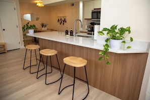 Une cuisine moderne avec un plan de travail blanc, des tabourets en bois et des plantes en pot.