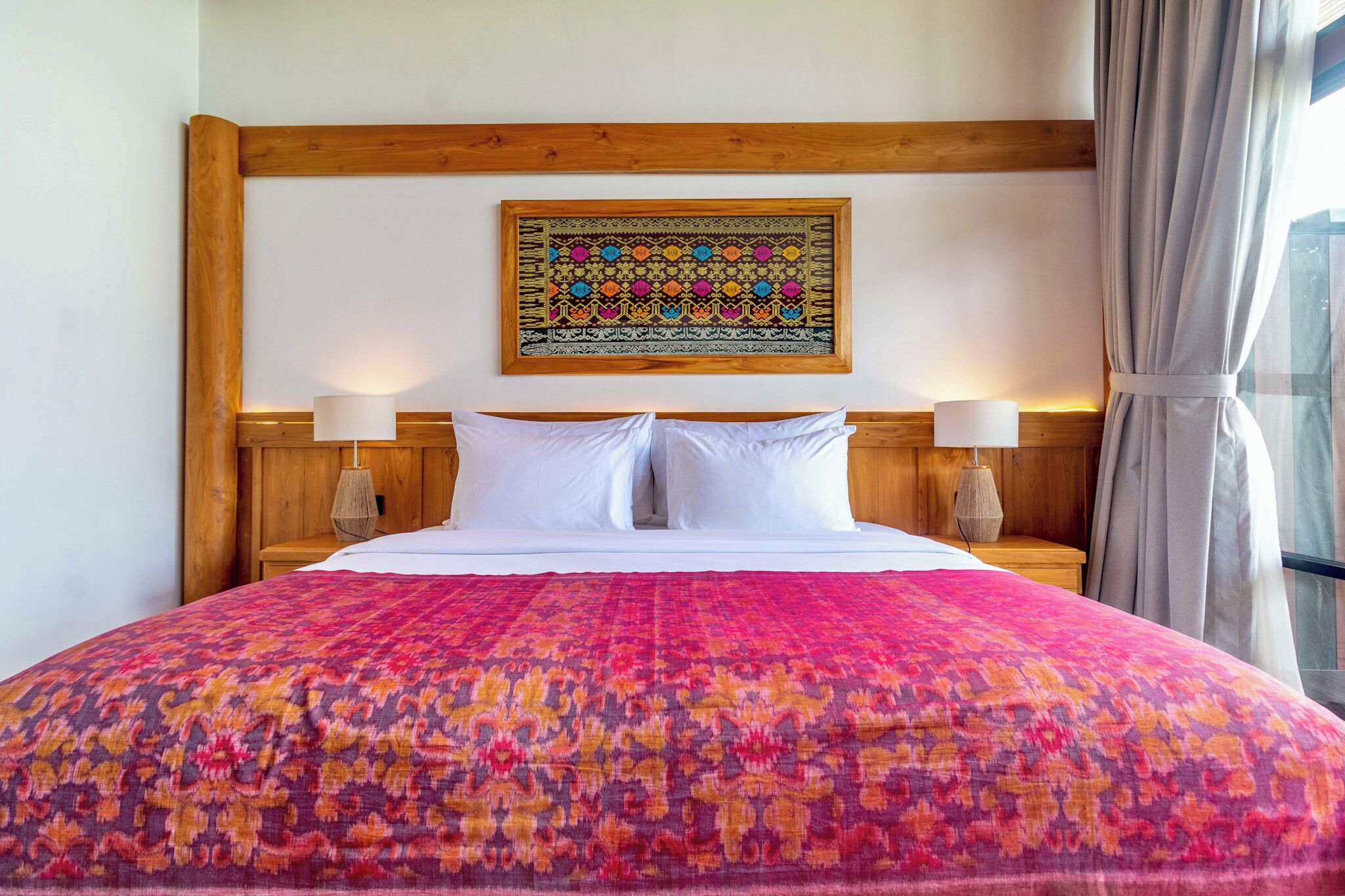 Una cama con una colcha estampada, dos lámparas de noche, un cabecero de madera y una obra de arte enmarcada en la pared.