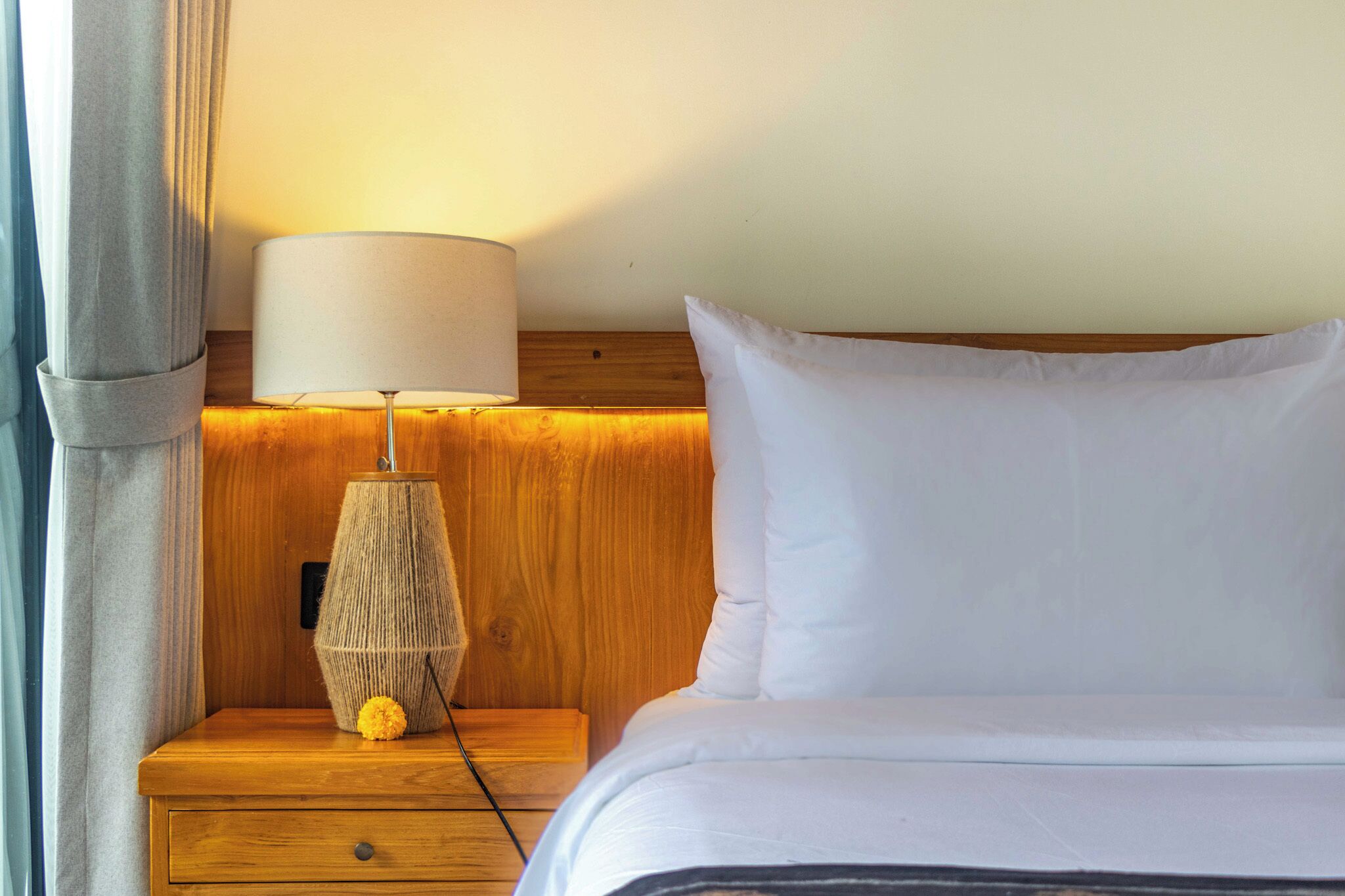 A neatly made bed with white bedding, a wooden nightstand with a lamp, and a small decorative item.