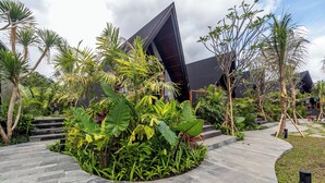 A modern building with a unique angular design, surrounded by lush tropical plants and a stone pathway. - Anandinii Resort Sidemen by AGATA (Sidemen)