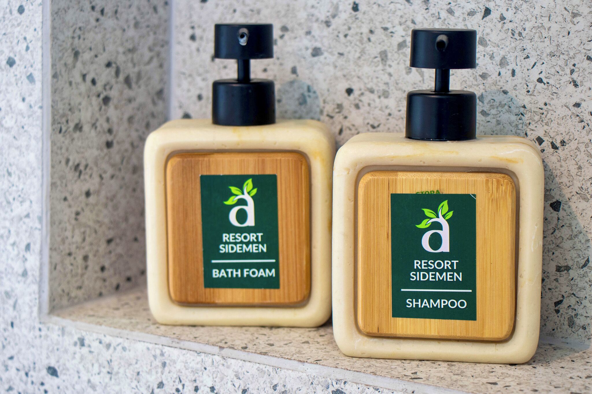 Two bottles of Resort Sidemen bath foam and shampoo on a speckled countertop.