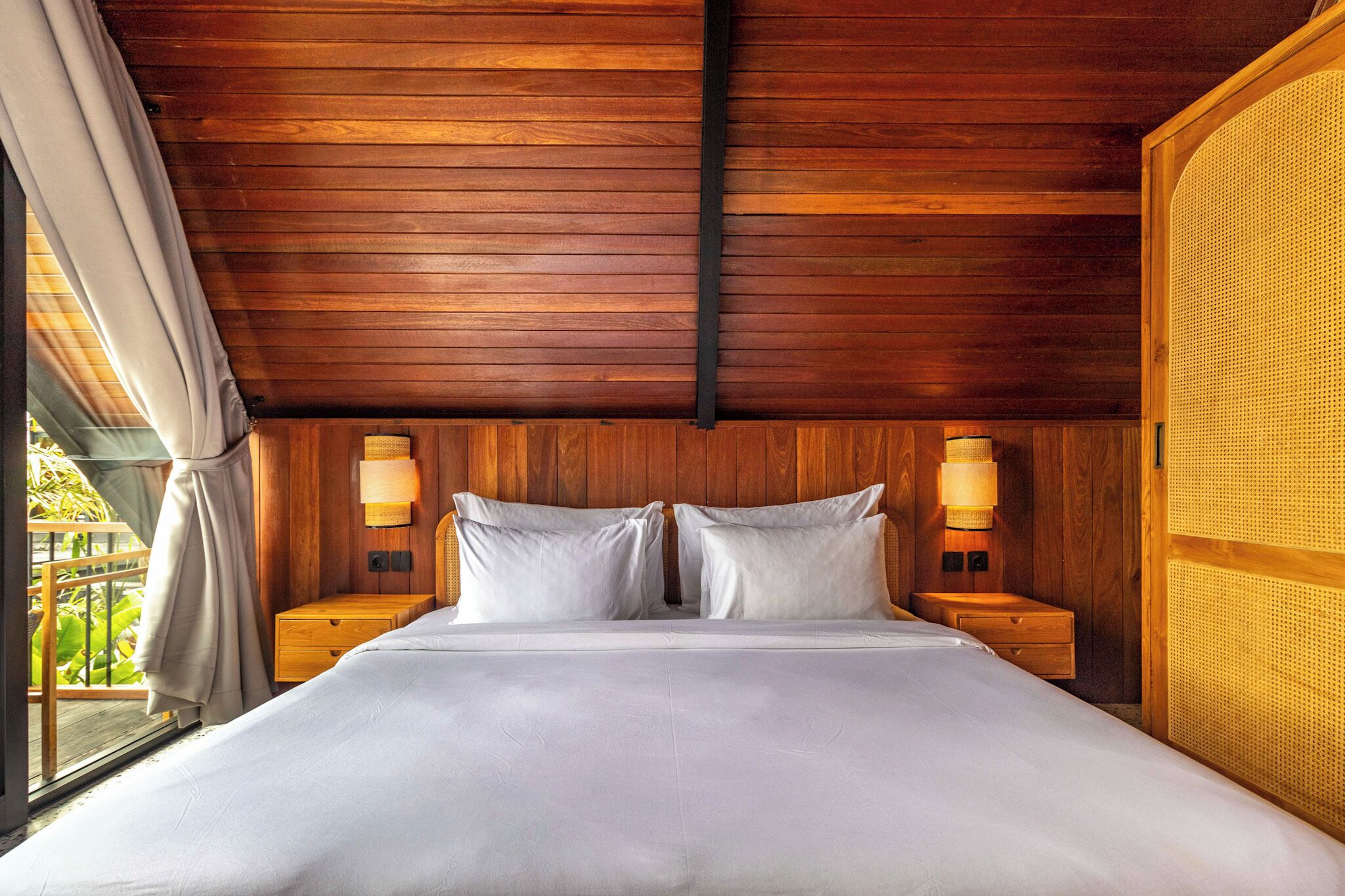 A wooden-paneled room with a bed, two bedside tables, and two wall-mounted lamps.