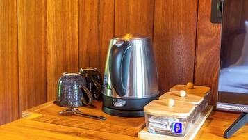 A kitchen area with a stainless steel kettle, a ceramic mug, a wooden tray with containers, and a digital clock.