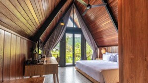 A wooden room with a bed, a table, and a view of greenery outside. - Anandinii Resort Sidemen by AGATA (Sidemen)