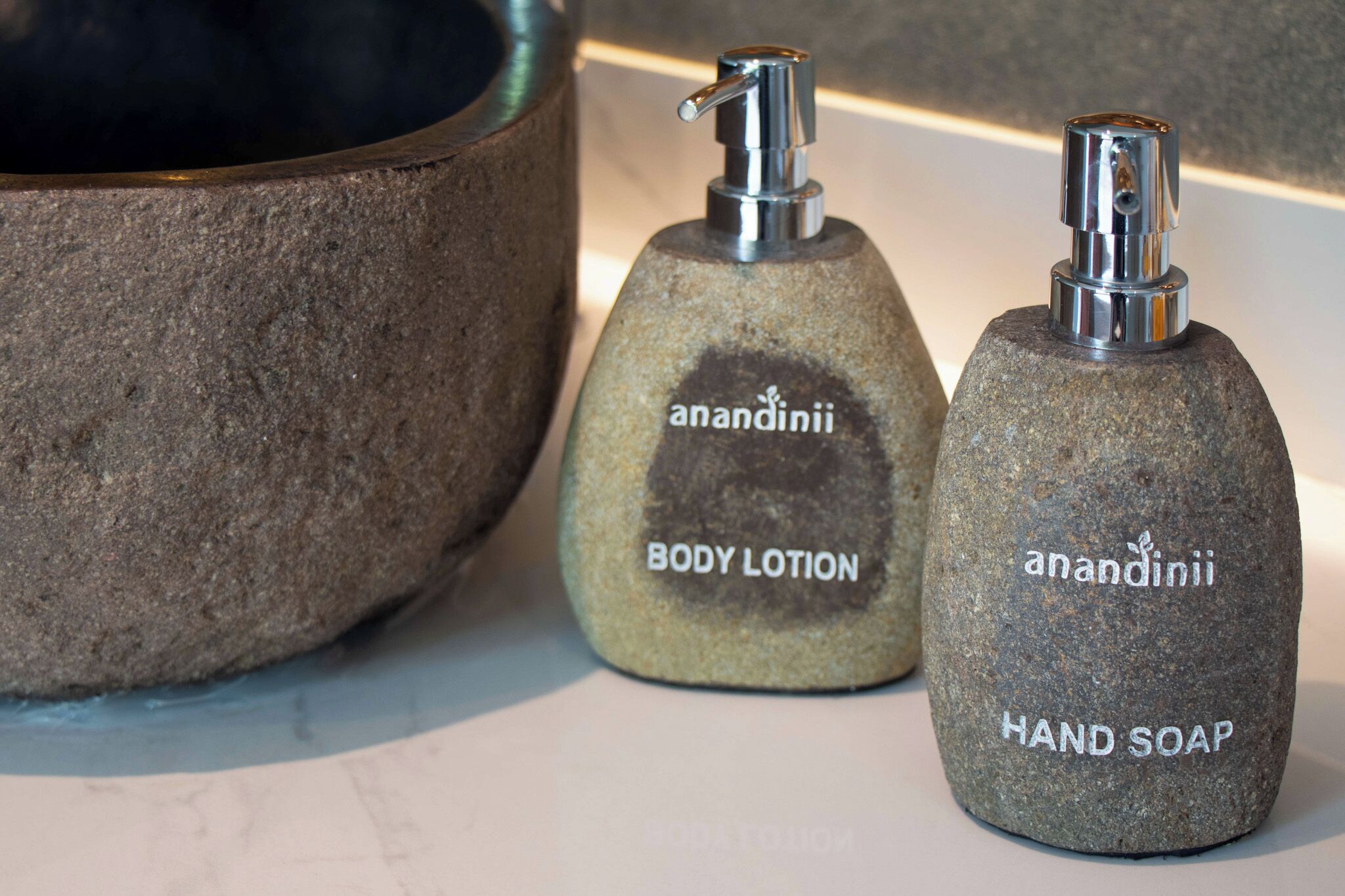 Two bottles of anandinii body lotion and hand soap on a stone surface.