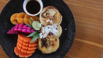 Un plato de panqueques, un cuenco pequeño de jarabe y diferentes adornos.