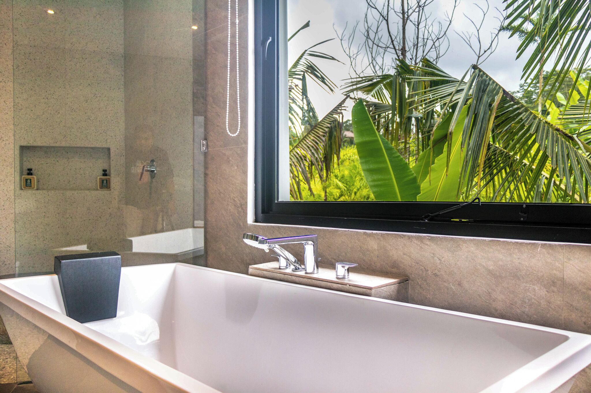 Un baño moderno con una bañera grande, un espejo y vistas a follaje tropical.