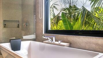Un baño moderno con una bañera grande, un espejo y vistas a follaje tropical.