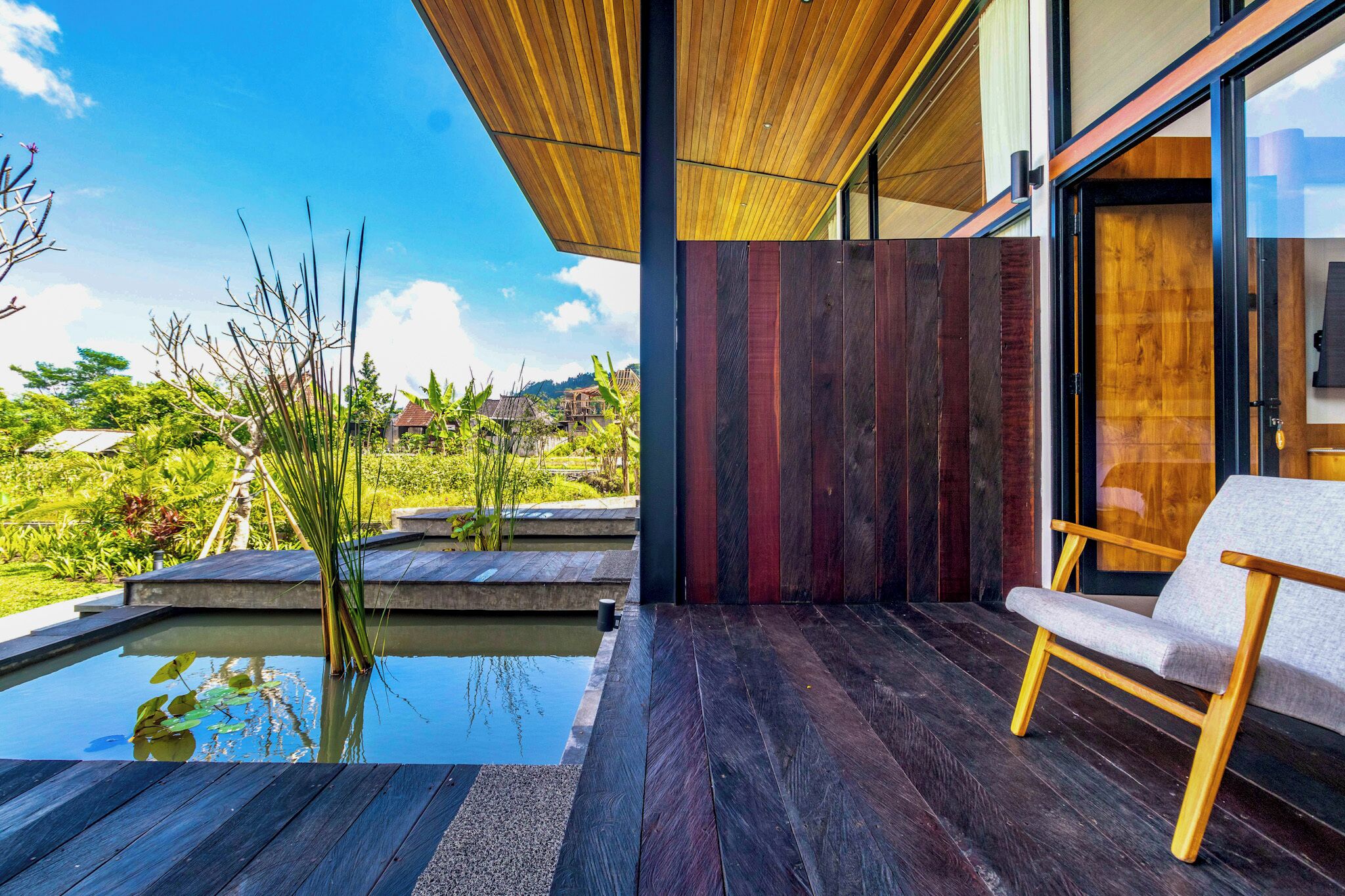 A modern interior with a wooden ceiling, a wooden bench, and a view of a garden with a water feature.