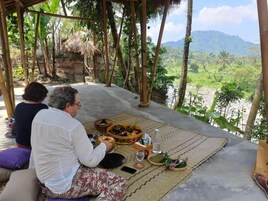A covered outdoor dining area with a view of a lush landscape, a table with food and drinks, and a person using a smartphone.
