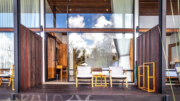 A modern interior with large glass windows, wooden flooring, and a seating area with chairs and a table. - Anandinii Resort Sidemen by AGATA (Sidemen)