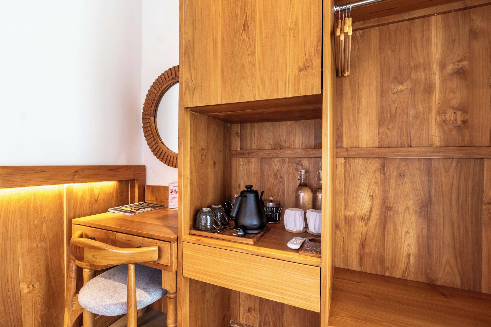 A wooden kitchenette with a wooden chair, a small table, a kettle, a coffee pot, and a microwave.