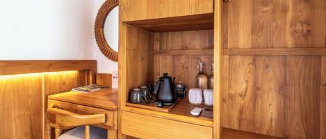 A wooden kitchenette with a wooden chair, a small table, a kettle, a coffee pot, and a microwave.