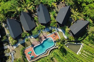 An aerial view of a resort with a swimming pool, multiple umbrellas, and lush greenery.