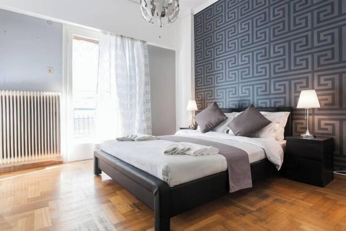 A bedroom with a bed, two bedside tables with lamps, a radiator, and a patterned wall.